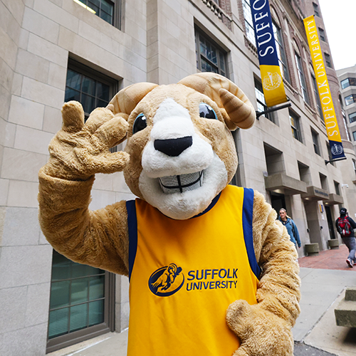 Suffolk mascot Rammy waves in front of a building on campus.