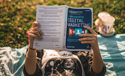 Close up of a woman reading a marketing textbook while lying on the grass
