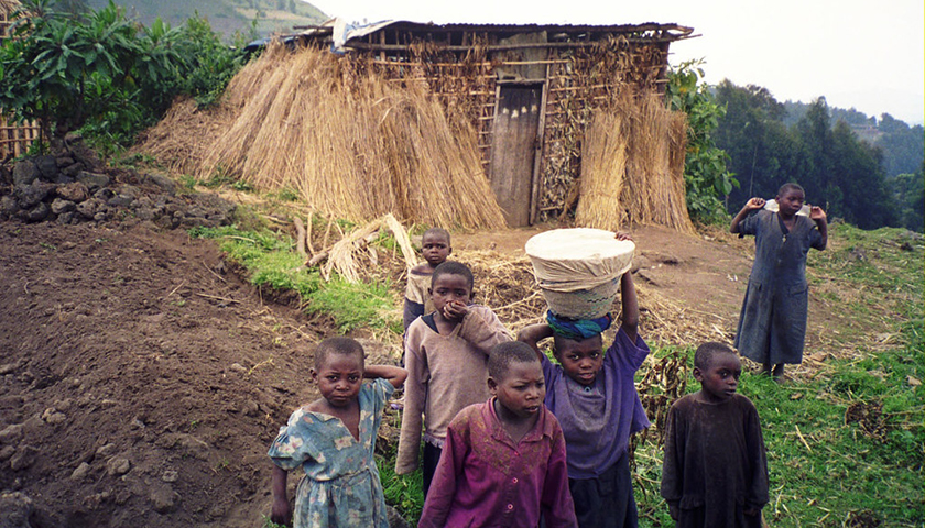 Children walking, one balancing cloth-wrapped container ion her head, with thatched building behind them