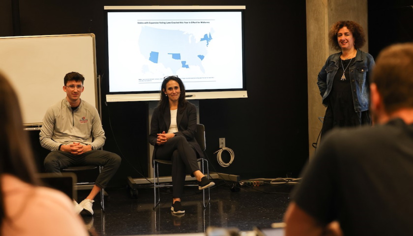A student, Professor Cobb, and Professor Madoni-Gerber take questions from the front of a journalism classroom with a powerpoint presentation in the background, slide titled "voting rights"
