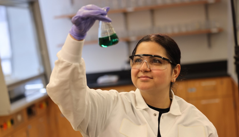 Sarah Bicalho in safety glasses examining a beaker of blue solution