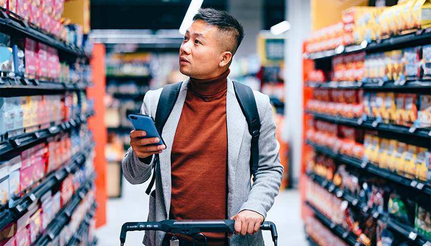 Man pushing shopping cart in grocery store aisle, a worried look on his face