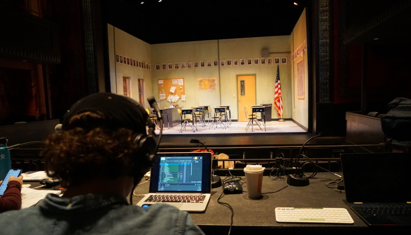 Facing the stage, set for the play 'Exception to the Rule' at the Modern Theatre. In the foreground, a student works on the technical aspects on a laptop.