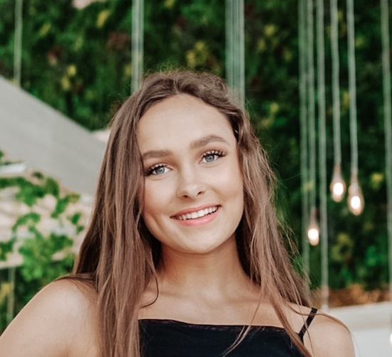 portrait of Skylar Billingsley smiling in front of a wall of greenery and hanging lights