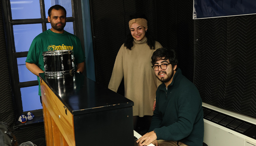 Andoreni Bustos plays the piano while Khalid Alkhalid and Sasha Meliefste watch