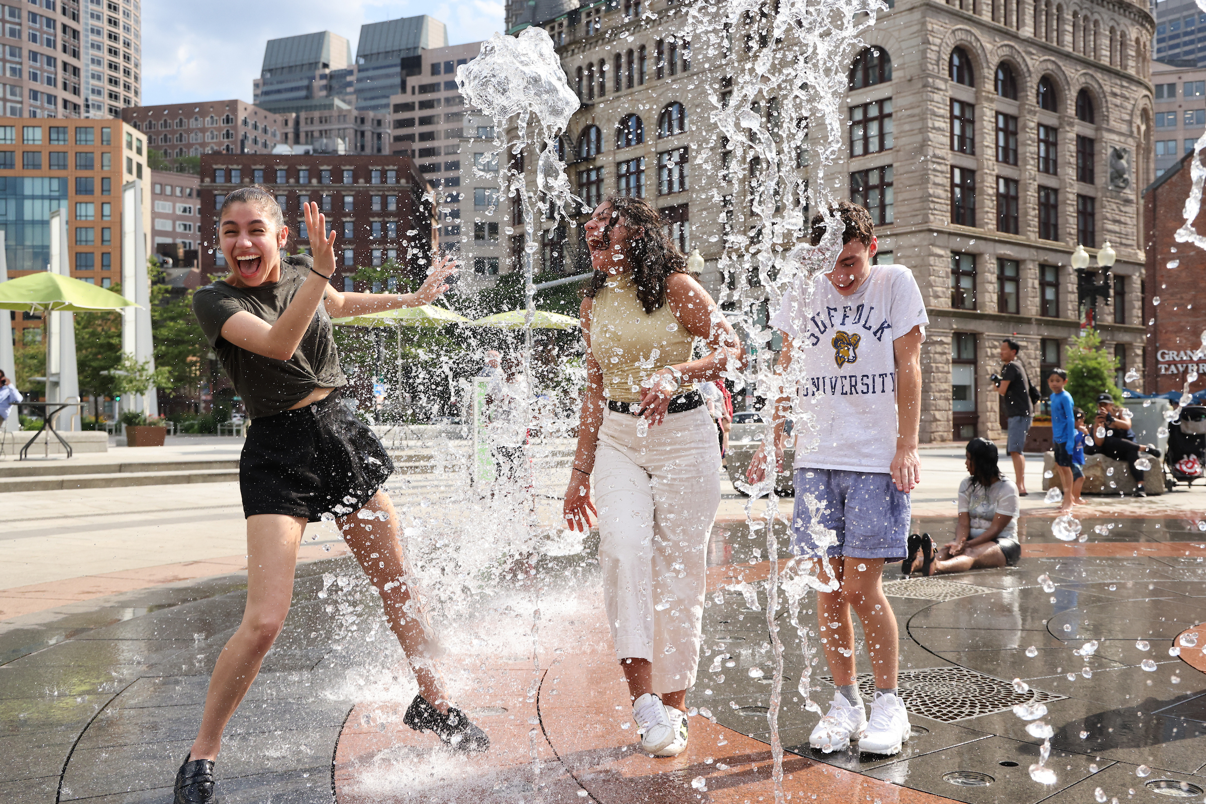 Suffolk undergrads Lucia Vilches, Class of 2024, Yasmine Tebib, Class of 2022, and Logan Gozzi, Class of 2024 enjoy a water fountain on a hot summer day in downtown Boston