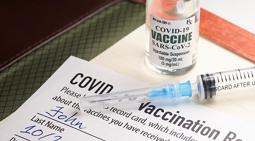 Vial of COVID vaccine and needle atop a COVID vaccination card