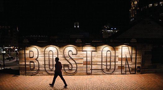 Person walking in front of Boston sign at night