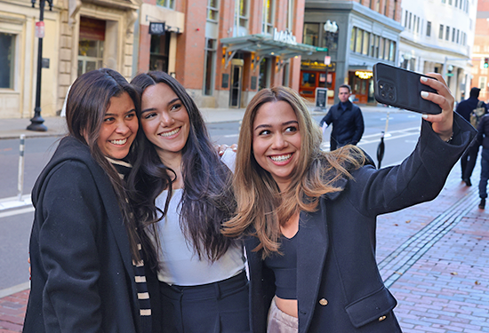Three Suffolk students take a selfie together on Tremont street on campus.