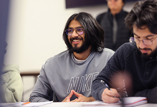A Suffolk student smiles off-camera while sitting among his peers in a math class.