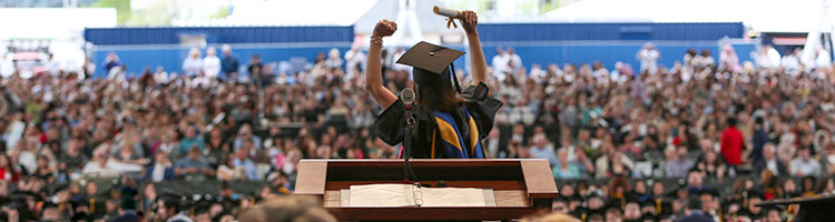 Student raises her hands as she receives diploma at Commencement