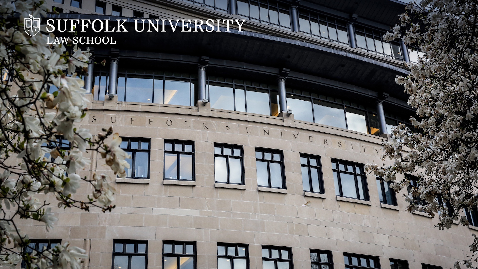 Sargent Hall with flowering trees in bloom in front of it with the Suffolk Law logo in the top corner