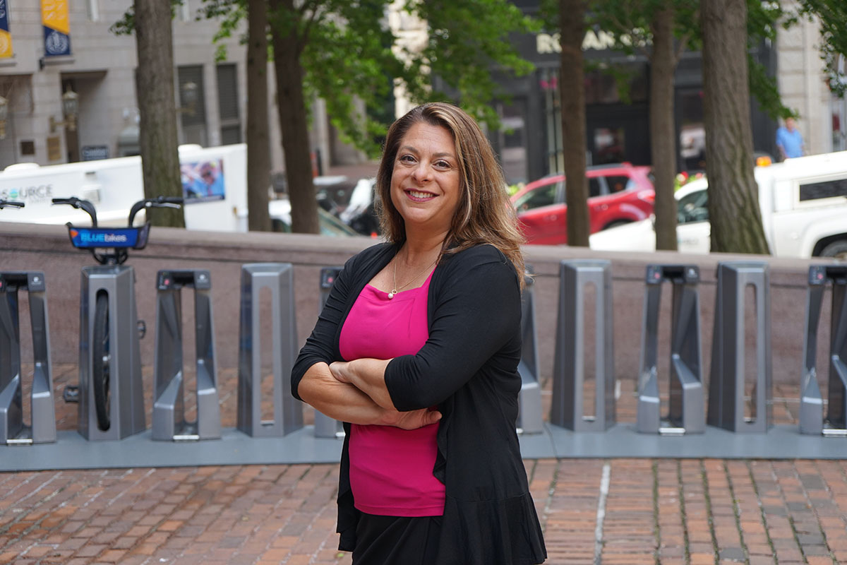 Michelle Quinlan standing outside, smiling with arms crossed, with blu sweater over pink shirt