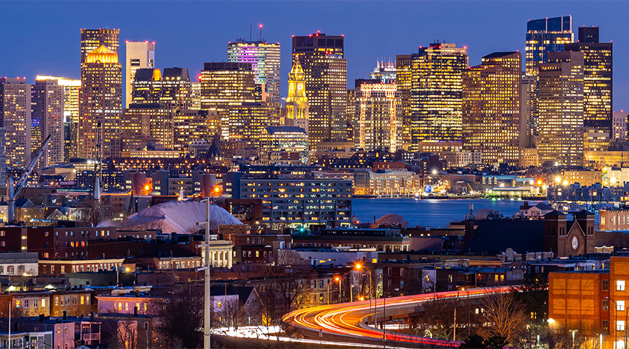 A nighttime skyline view of Boston, with the city lights twinkling off the river.