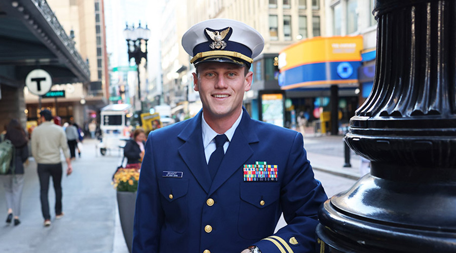 A man in a Coast Guard uniform stands in Boston's Downtown Crossing with a public transport T sign behind him.