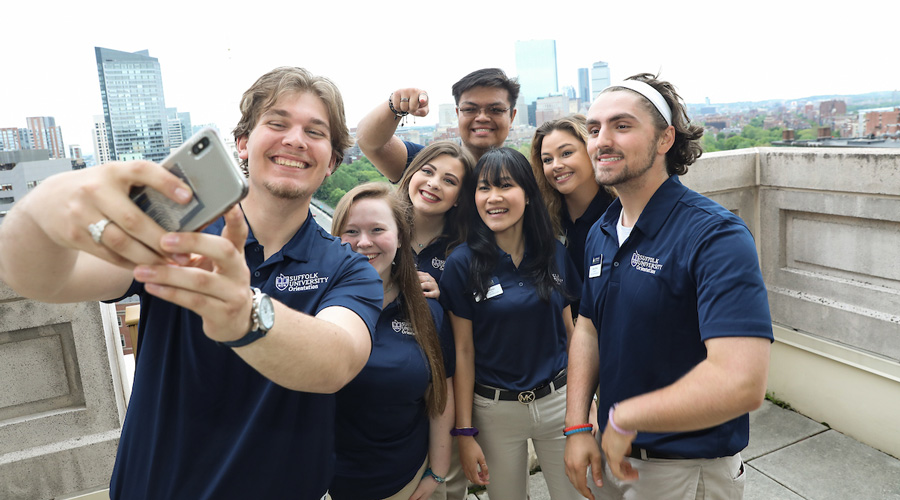 A group of Suffolk students pose for a photo on the 73 Tremont balcony overlooking the Boston skyline.