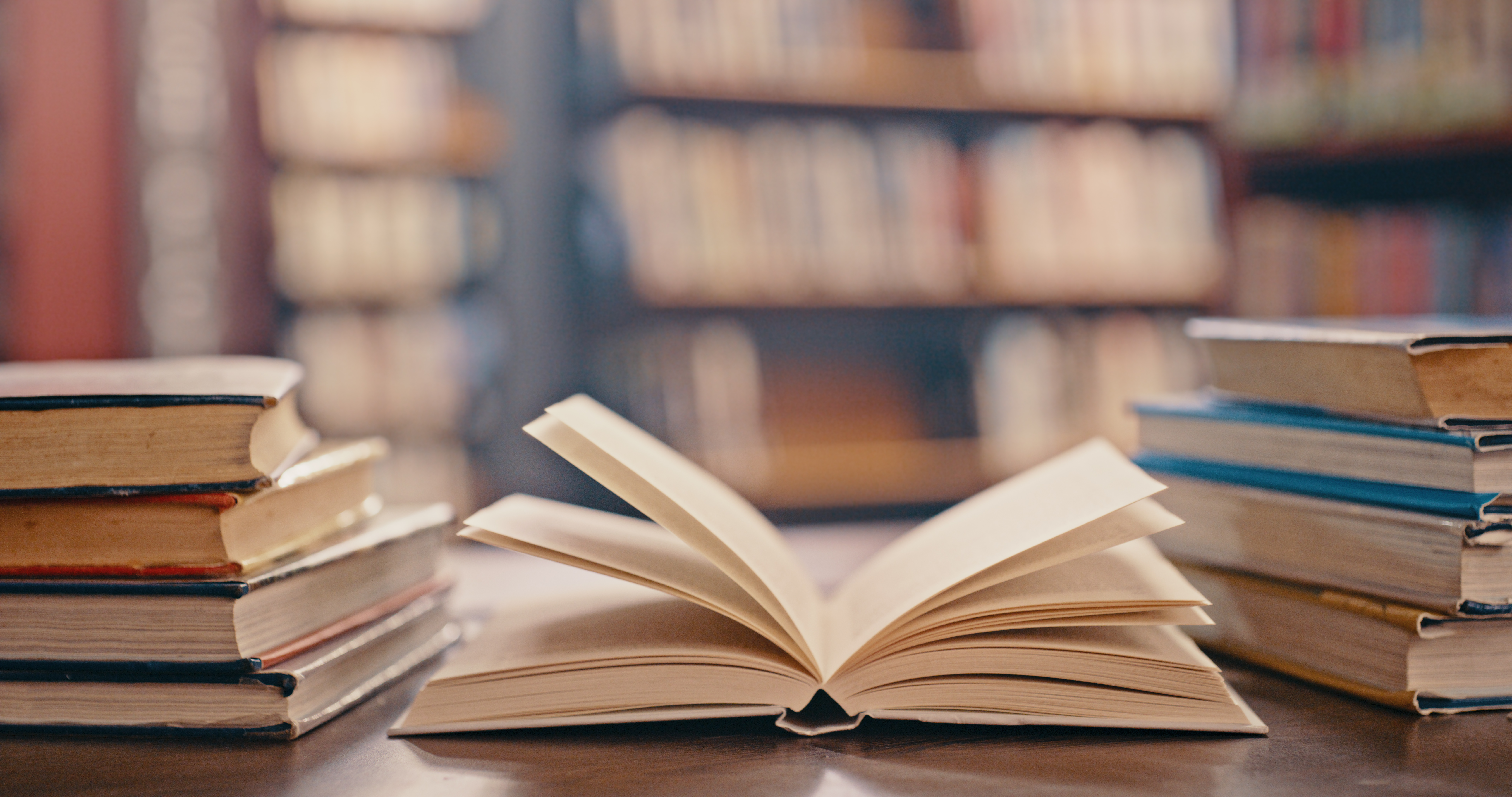Stock photo of a book open on a table surrounded by multiple stacked books