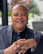 Portrait of Trustee Danny Best, smiling in grey suit jacket and hands crossed