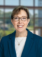 Trustee Dorothy Savarese smiling with navy blue blazer and white shirt, wearing glasses