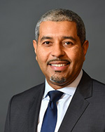 Portrait of Trustee Manny Lopes, smiling in black suit jacket and blue tie