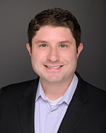 Portrait of Trustee Patrick Coelho, smiling in black suit jacket