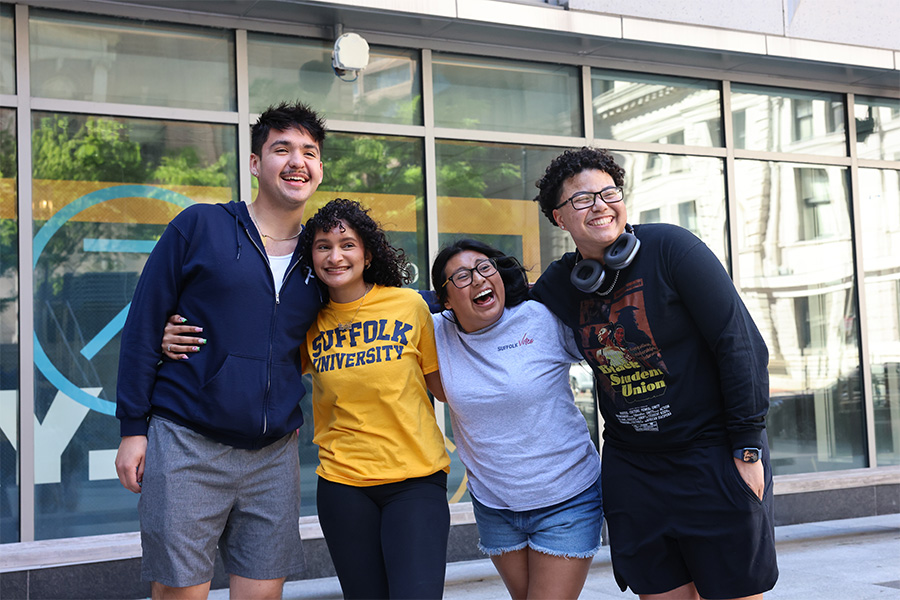 Suffolk students posing together arm-in-arm in front of a campus building.