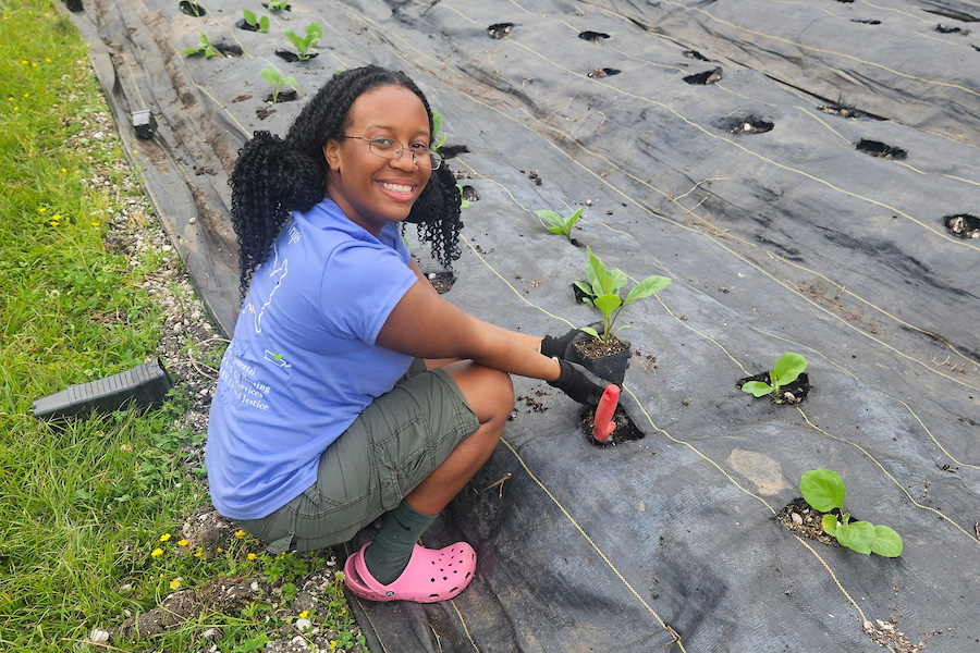 A Suffolk student crouching down to plant something in the round and smiling at the camera.