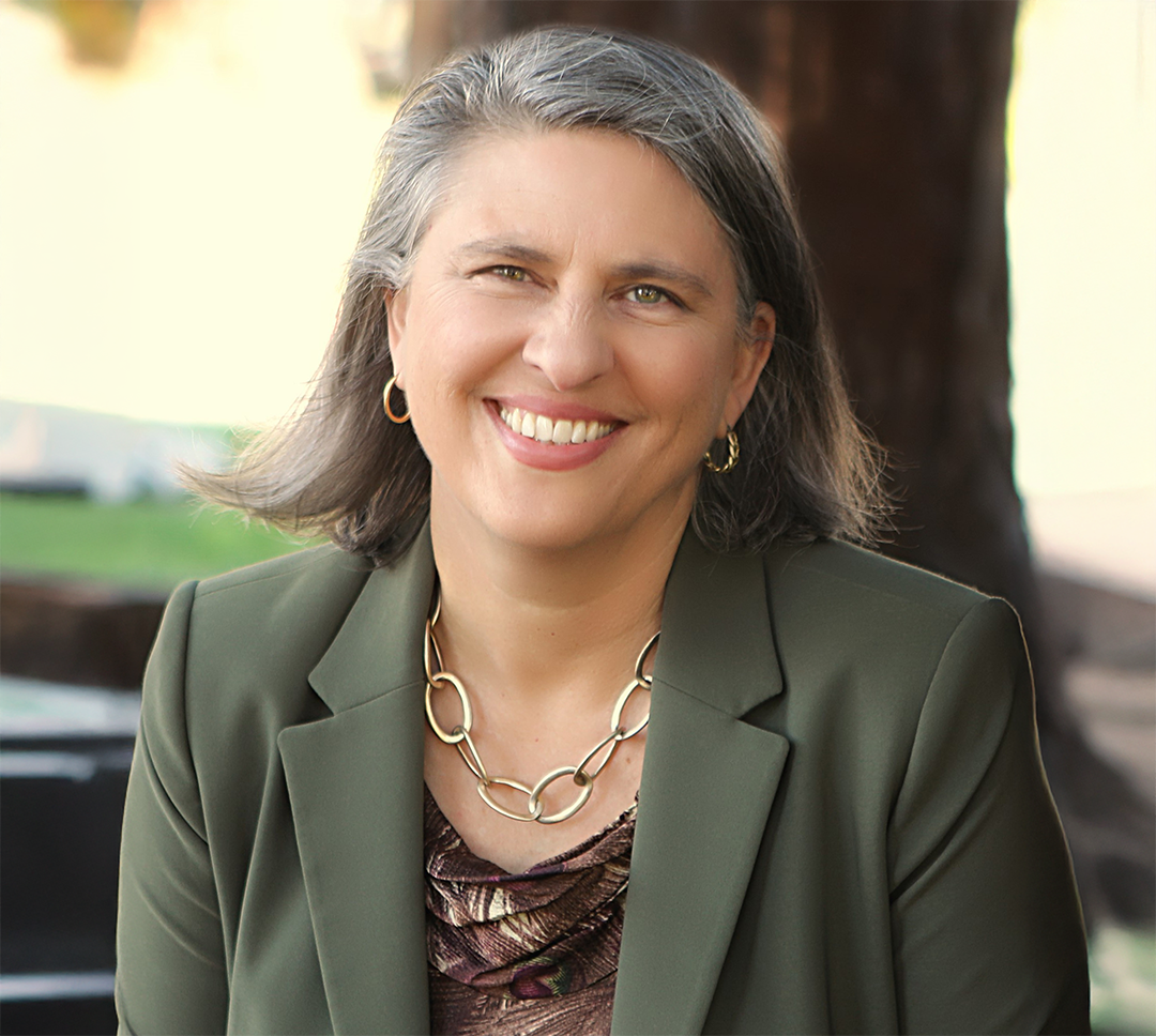 CAS Dean Edie Sparks smiles outdoors while wearing a green blazer.