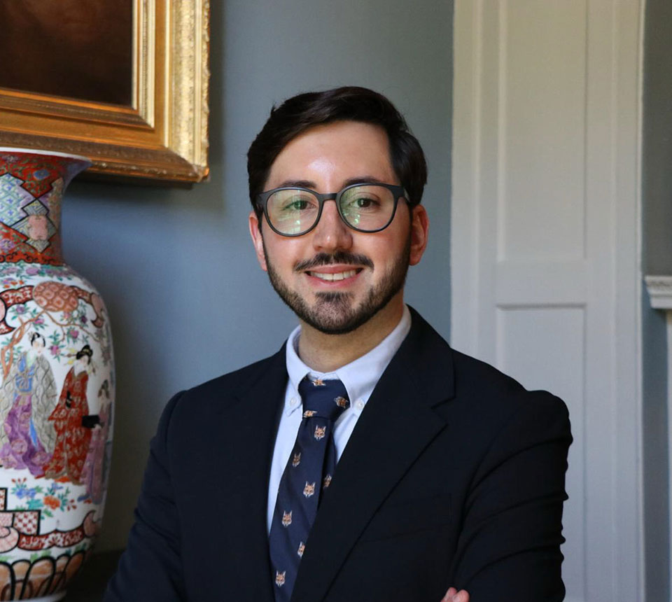 Héctor Linares, arms crossed standing next to bookcase
