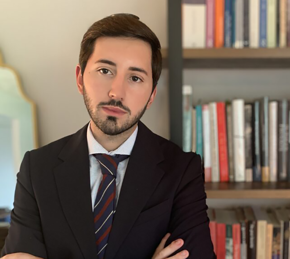 Héctor Linares, arms crossed standing next to bookcase