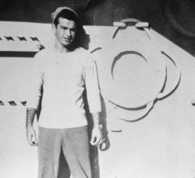 Young Moakley in the navy standing in front of a boat