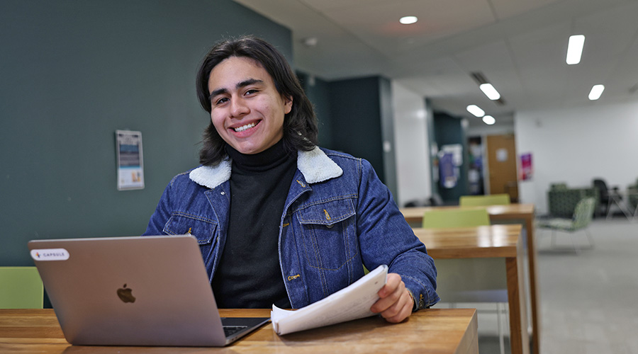 A Suffolk student sits at an outdoor table with his laptop.