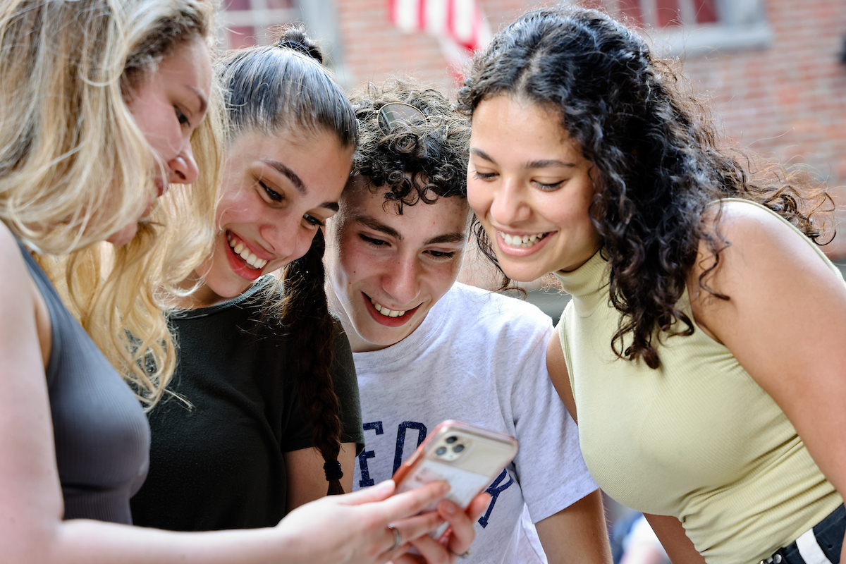 A group of Suffolk students leaning over to look at a central phone screen.