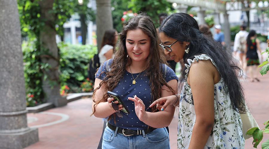 Two Suffolk students look down at one of their phone screens smiling in the Isabella Stewart Gardener Museum.