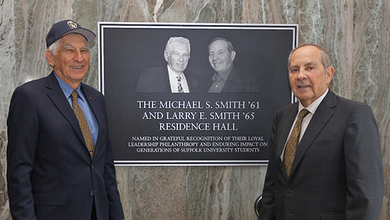 Michael & Larry Smith pose for a photo together in front of the dedication plaque in the Smith residence hall on campus. 