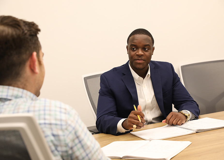 A Suffolk student in an interview sitting at a table in a conference room.