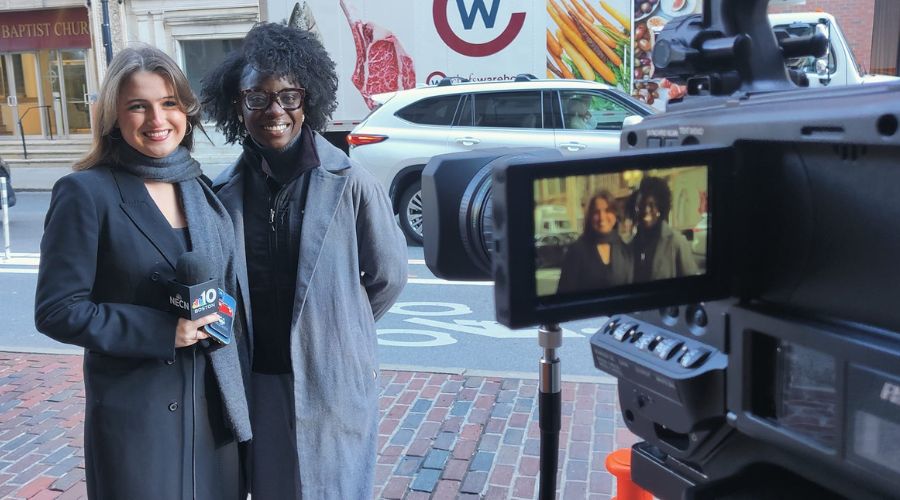 A Suffolk student holding a NECN news microphone stands in front of Suffolk's Studio 73.