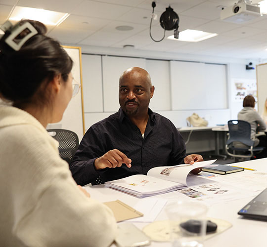 Student and preofessor sit at a table discussing the student's work