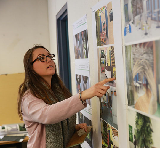 Student geturing at artwork hanging on a wall