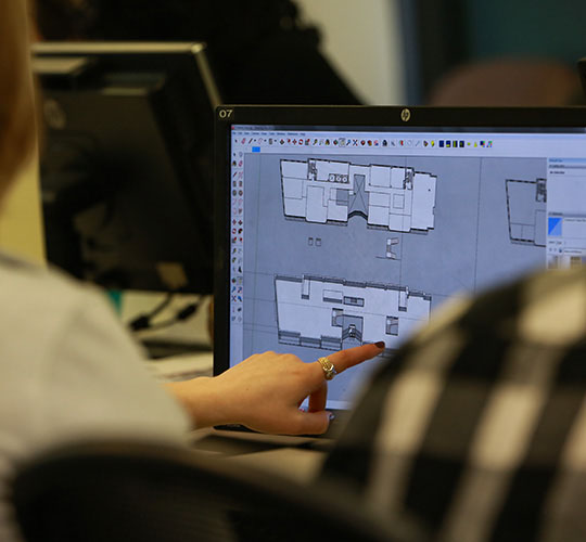 Student gesturing at laptop screen showing design/CAD software