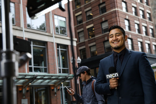 student smiling and broadcasting in front of Suffolk.