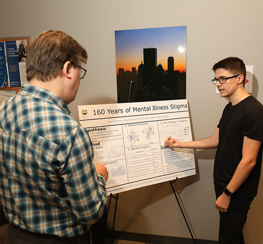 Student gestures at his presentation while explaining it to a professor