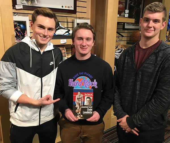 A group of students pose with a book titled "The Story of Basketball Great: Clyde Lovellette".