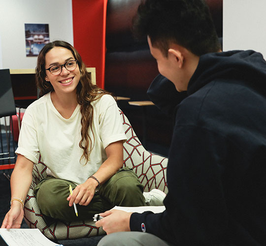 Two students facing each other and smiling as they work on a project