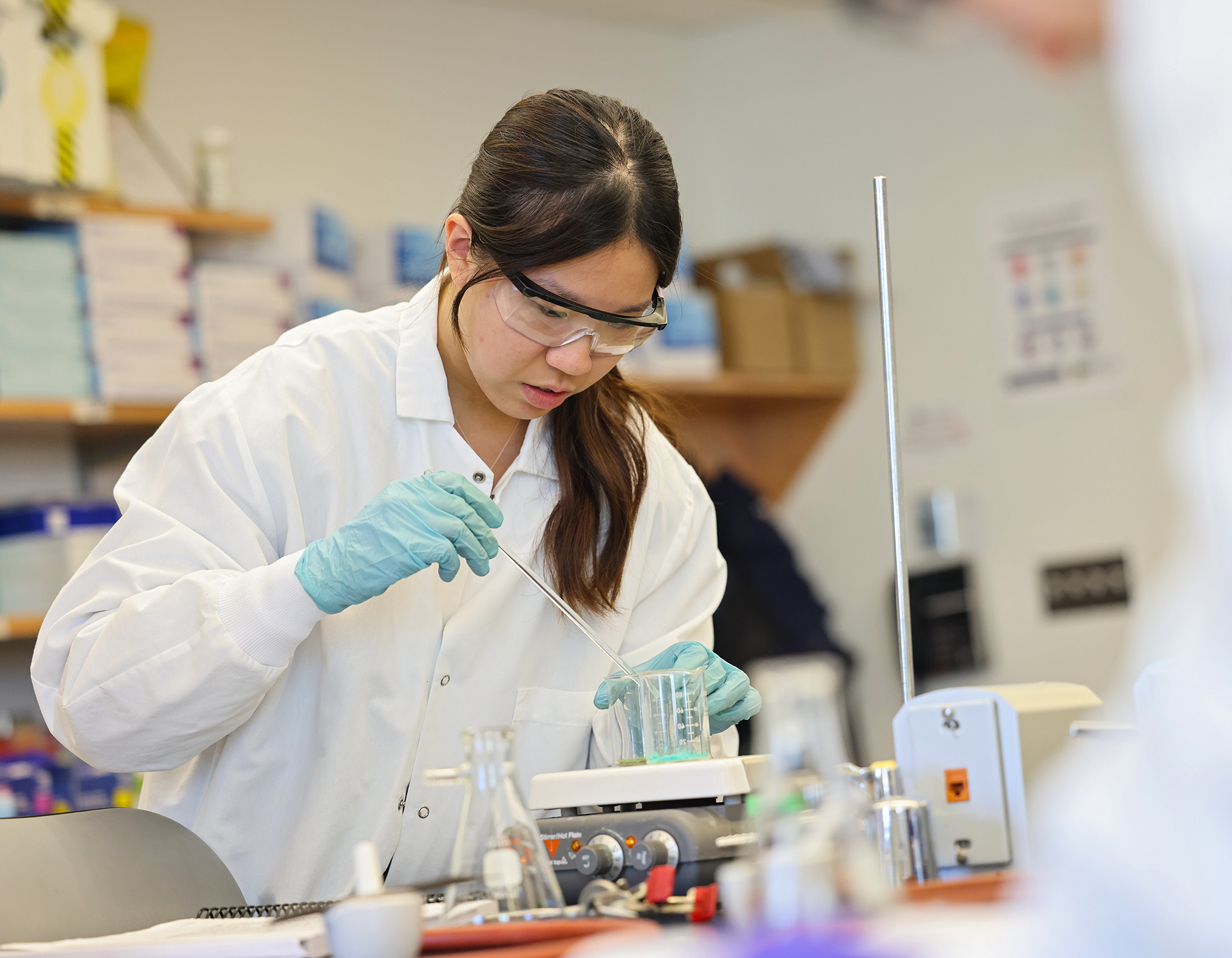 A Suffolk student in a lab coat and goggles during a lab class.