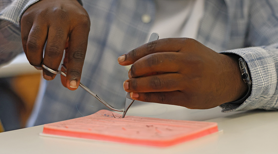 A closeup of a Suffolk student's hands while he participates in a suture clinic on campus.