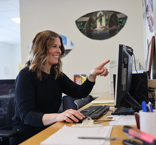 Student at a desk gesturing towards a conputer monitor