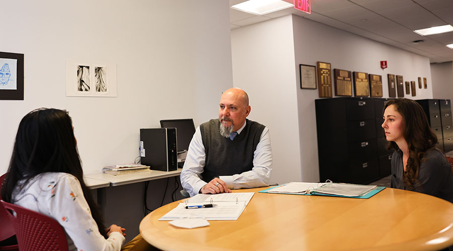 two students sit at a table with faculty member