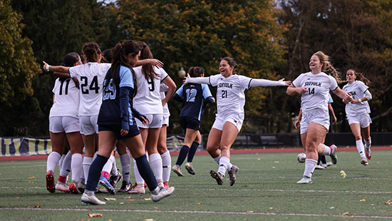 Women's soccer players celebrate on the grassy pitch.