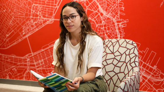 Suffolk student Gabriela poses for a portrait holding a notebook sitting in the INTO Suffolk lobby.